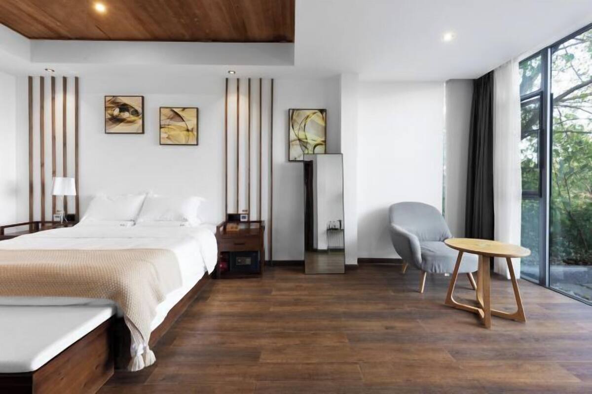Un dormitorio moderno con cama, mesitas de noche, una silla, una pequeña mesa y obras de arte en las paredes.