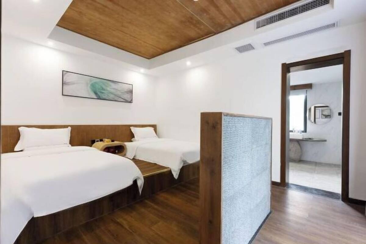 Habitación de hotel con dos camas, techo de madera, un cuadro en la pared y un baño visible a través de una puerta abierta.