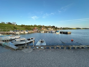 Een haven met stilgelegde boten, een grindpad en huizen op de achtergrond.