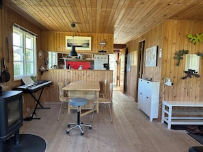 L’intérieur d’un chalet en bois comprend une table à manger, des chaises, un piano et un coin cuisine.