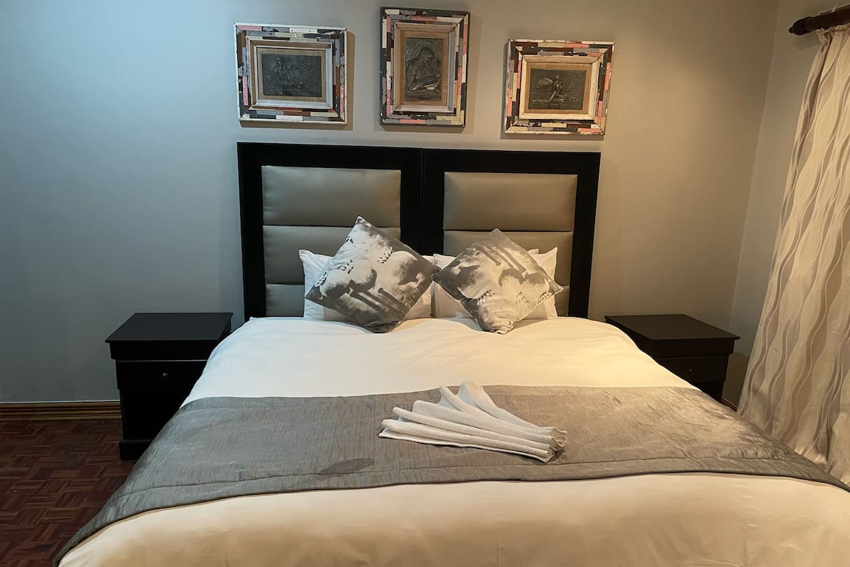 Una cama bien hecha con cabecera, dos mesitas de noche y tres cuadros enmarcados en la pared.