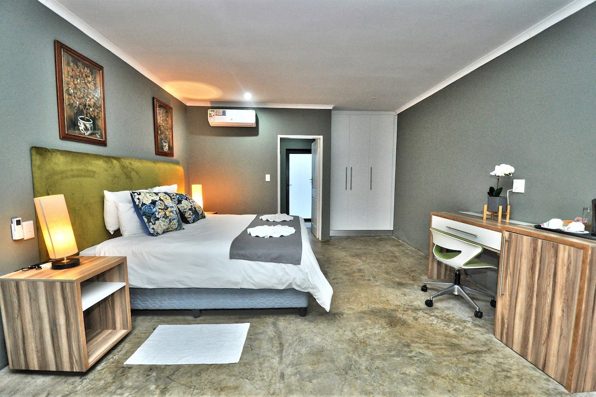 Una habitación de hotel moderna con cama, mesita de noche, escritorio y armario.