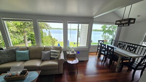 A living room with a sofa, a dining table with chairs, and large windows overlooking a body of water. - Beautiful lakefront property on Barton Lake with Hot Tub! (Vicksburg)