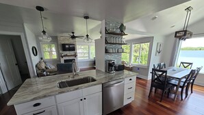 A modern kitchen with a large island, white cabinetry, a built-in oven, and a dining area with a view of the outdoors. - Beautiful lakefront property on Barton Lake with Hot Tub! (Vicksburg)