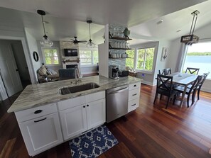 A modern kitchen with a large island, white cabinetry, a built-in oven, and a dining area with a view of the outdoors.