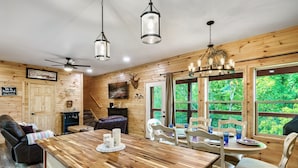 Ein Holzhütten-Interieur mit Essbereich, Kamin und großen Fenstern mit Blick auf den Wald.