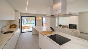Et moderne køkken med en stor ø, indbygget ovn og havudsigt gennem skydedøren.