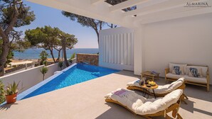 Ein moderner Poolbereich im Freien mit Blick aufs Meer, einer Steinmauer und einer Holzliege.