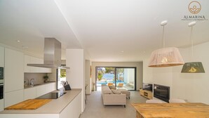 Eine moderne Küche mit einer großen Kochinsel, ein Essbereich mit einem Holztisch und ein Wohnzimmer mit Sofa und Fernseher.