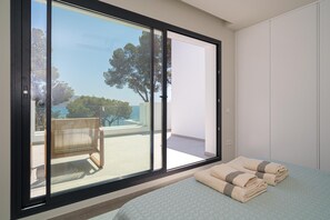 A bedroom with a large sliding glass door leading to a balcony with a chair and a view of the sea. - Balilos 4 - By Almarina Villas (Moraira)