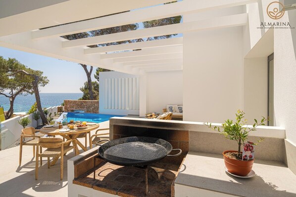 A terrace with a stone table, chairs, a grill, a potted plant, and a view of the sea. - Balilos 4 - By Almarina Villas (Moraira)