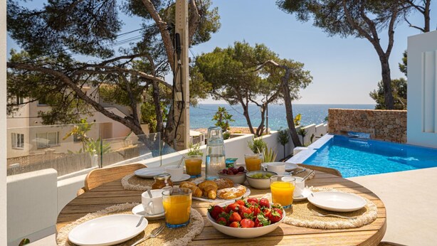 Ein Esstisch mit Blick auf einen Swimmingpool und das Meer.