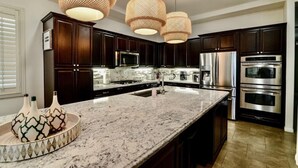 Cozinha moderna com armários de madeira escura, eletrodomésticos de aço inoxidável, bancada de granito e três luminárias pendentes de fibra.