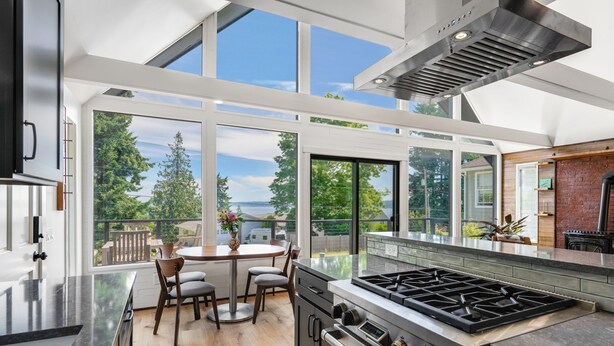A modern kitchen with a large island, stainless steel appliances, and a view of the outdoors. - Renovated A-frame with water view (Vashon)