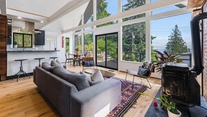 A spacious living area with a large sofa, a fireplace, and a view of the outdoors. - Renovated A-frame with water view (Vashon)