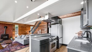 A modern kitchen with a central island, stainless steel appliances, and a wooden accent wall. - Renovated A-frame with water view (Vashon)