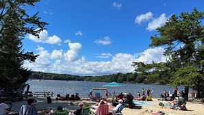 A lakeside beach with people relaxing on chairs and sunbathing.
