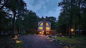 A two-story log cabin with a stone chimney, surrounded by a forest.