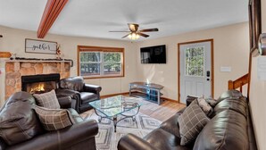 A living room with a fireplace, leather sofas, a glass coffee table, and a ceiling fan.