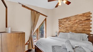 A bedroom with a wooden headboard, a bed with white linens, a wooden cabinet, and a window with curtains.