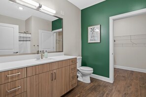 A bathroom with a wooden vanity, a white toilet, and a green accent wall. - The Rodeo Drive Suite Penthouse The Gulch (Nashville)