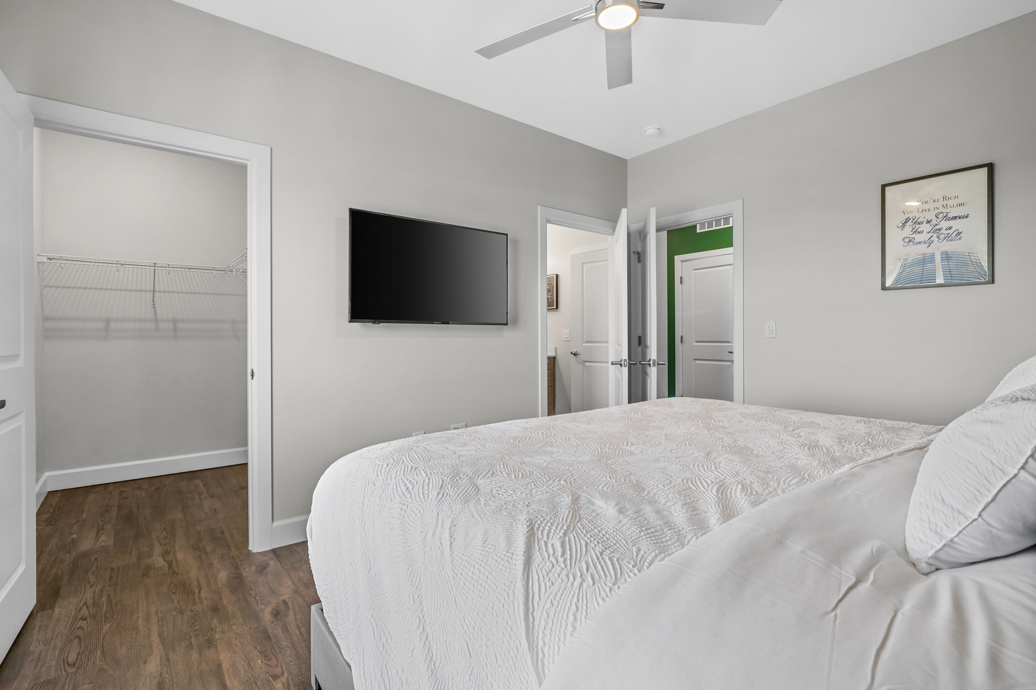 Una camera da letto con un letto, una ventola a soffitto, una TV e una citazione incorniciata al muro.