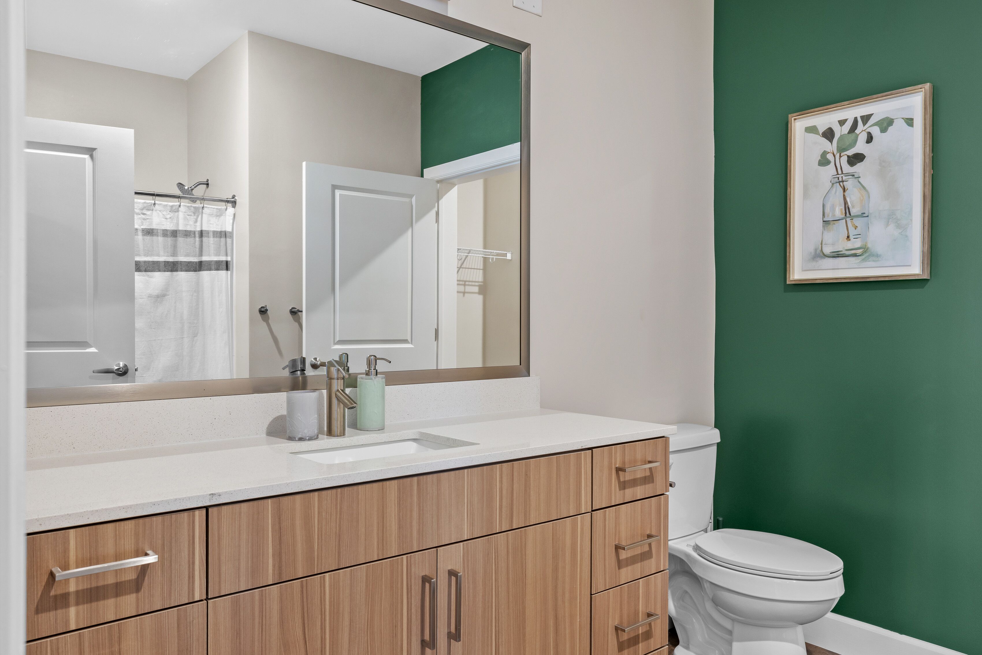 A bathroom with a white sink, wooden cabinets, a white toilet, and a green wall.