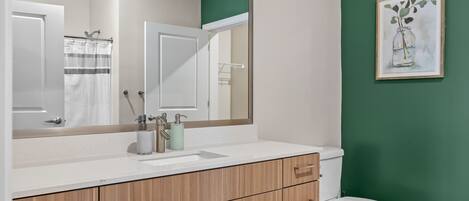 A bathroom with a white sink, wooden cabinets, a white toilet, and a green wall.