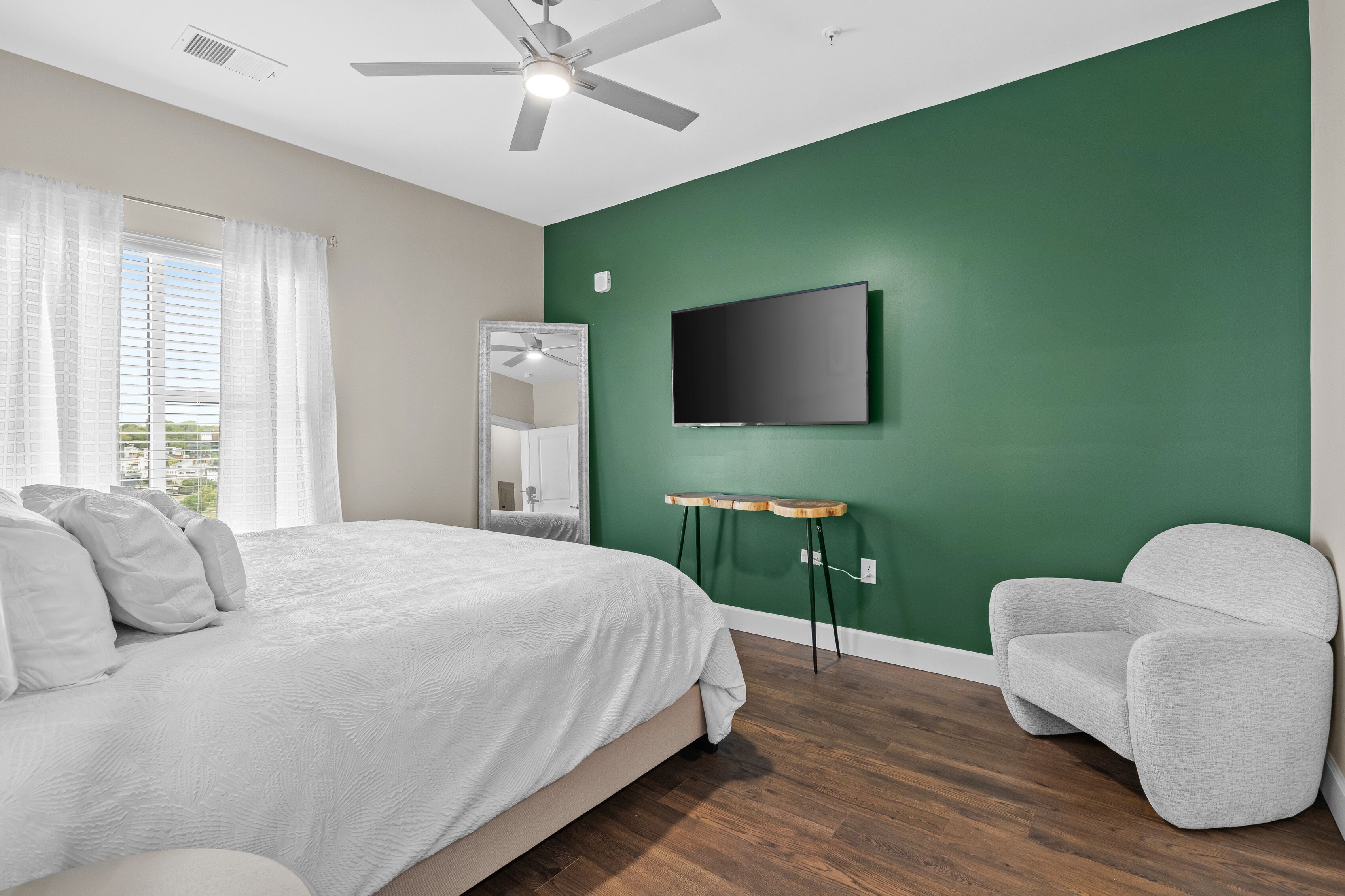 A bedroom with a bed, a TV mounted on the wall, a chair, and a small table.