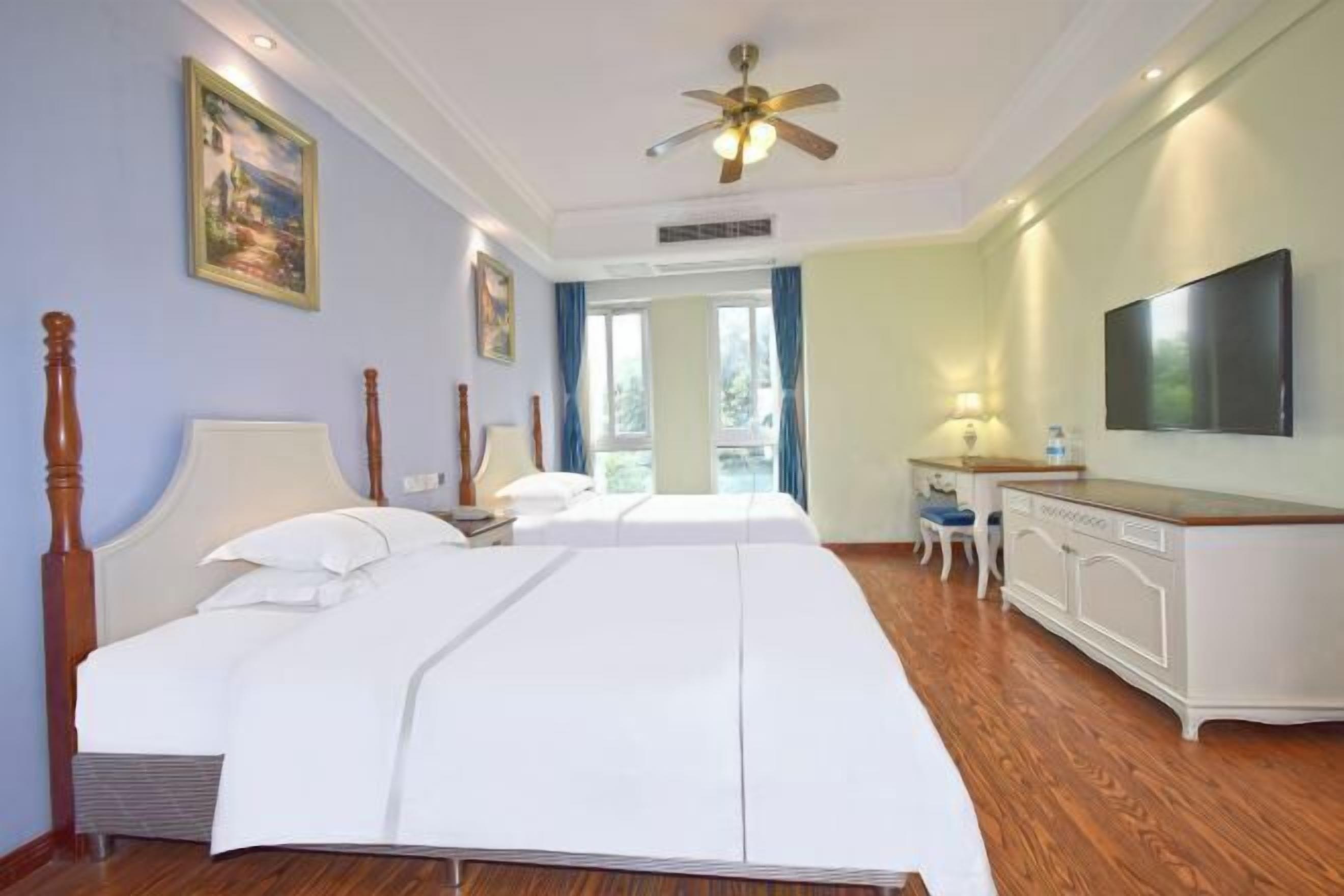 A hotel room with a large bed, a desk, a television, and a ceiling fan.