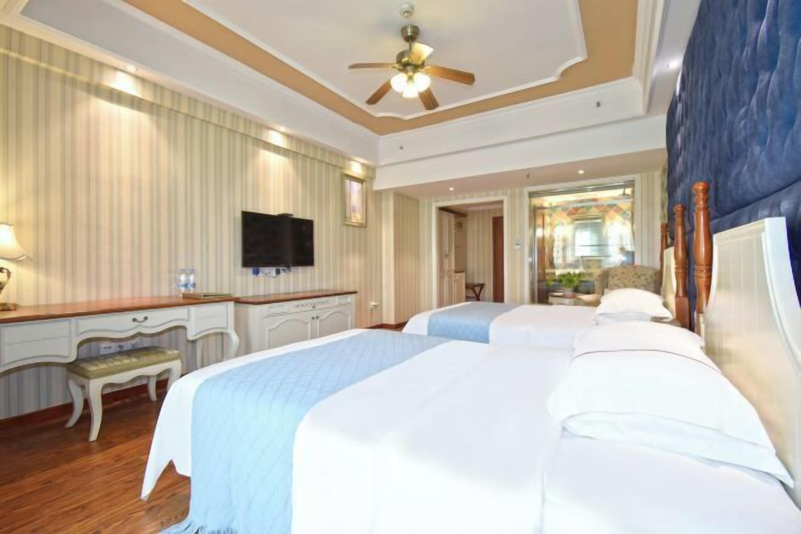 Habitación de hotel con dos camas, un escritorio, una silla, un televisor y un ventilador de techo.