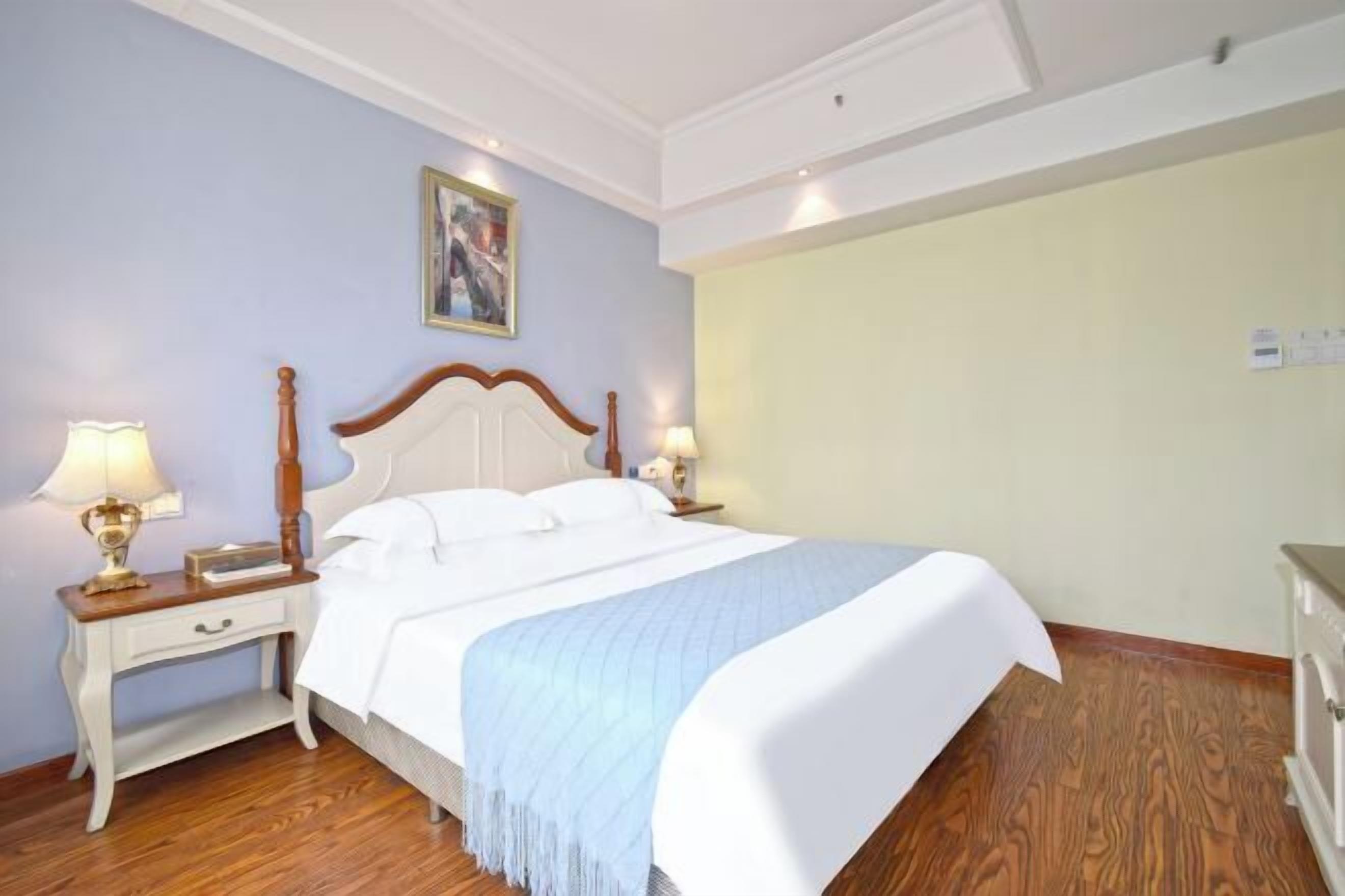 A neatly arranged bedroom with a large bed, two bedside tables with lamps, and a painting on the wall.