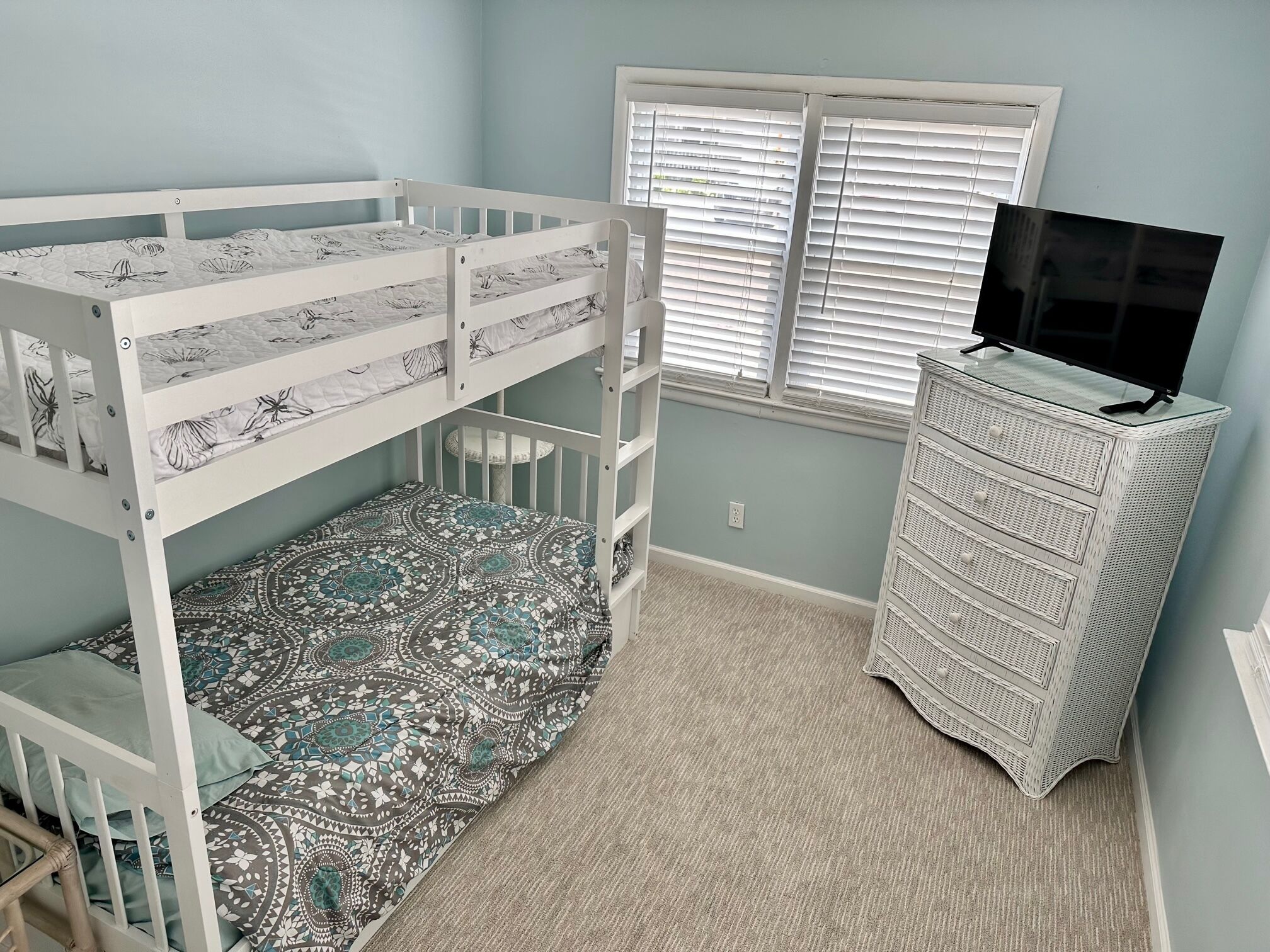 A room with a bunk bed, a dresser, and a window with blinds.