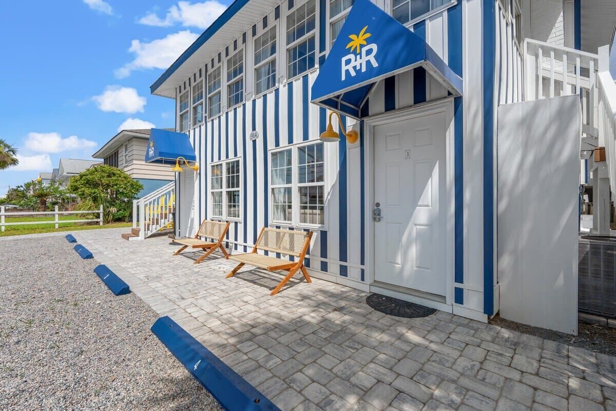 Un edificio con una facciata blu e bianca, un cartello con il logo 'R&R' e due sedie di legno all'esterno.