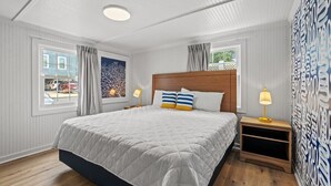 A bedroom with a large bed, two bedside tables with lamps, a window with curtains, and a patterned wall.