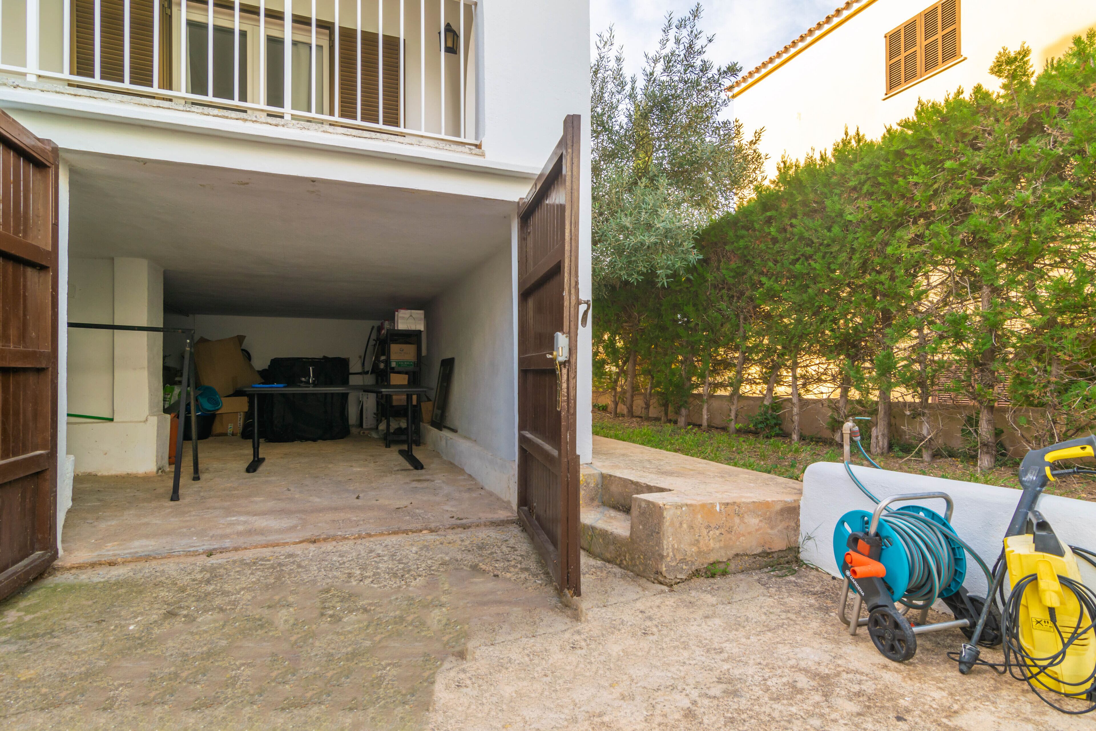A garage with a table and chairs, a ladder, and a hose reel outside.