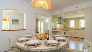 A dining area with a round table set for six, surrounded by chairs. A basket of fruit and bottles of wine are on the table. - VILLA BLANCA - Beautiful villa with private swimming pool and free WIFI (Felanitx)