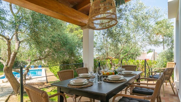An outdoor dining area with wicker chairs and a table set for a meal, overlooking a pool and trees. - VILLA BLANCA - Beautiful villa with private swimming pool and free WIFI (Felanitx)