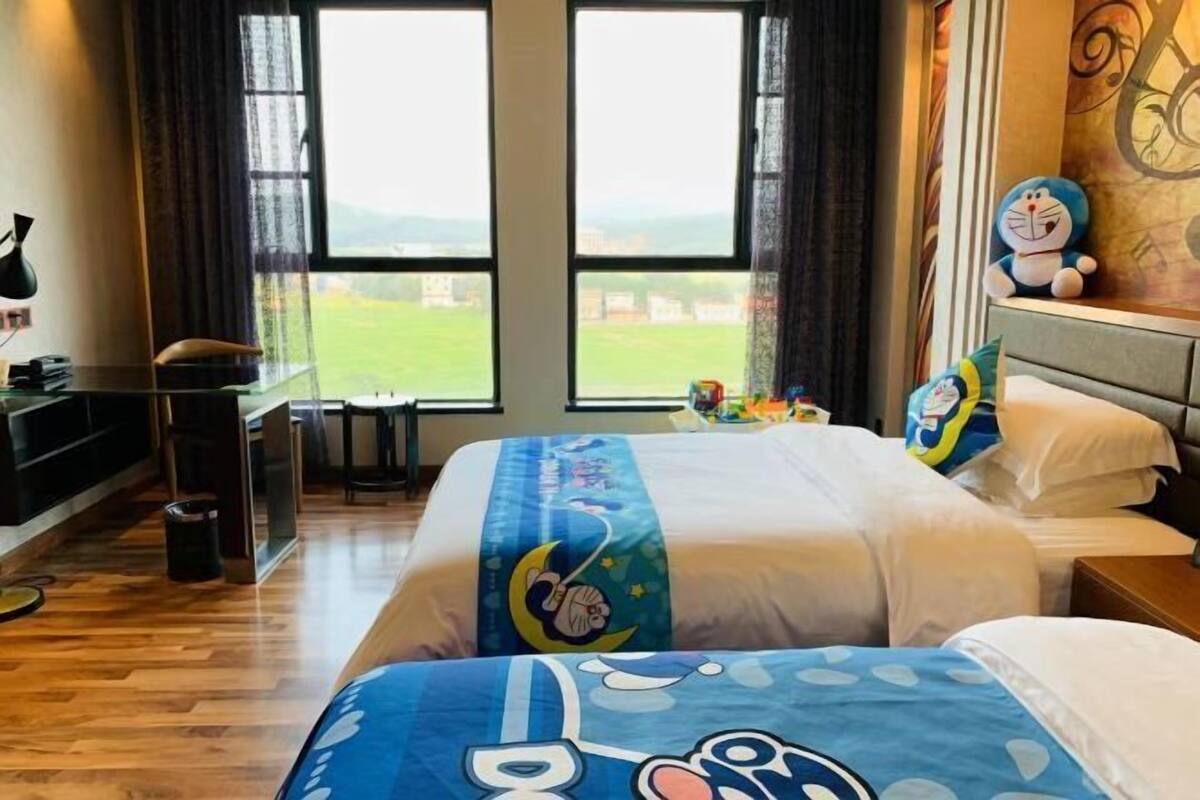 A hotel room with two beds, a desk, and a view of the outdoors.