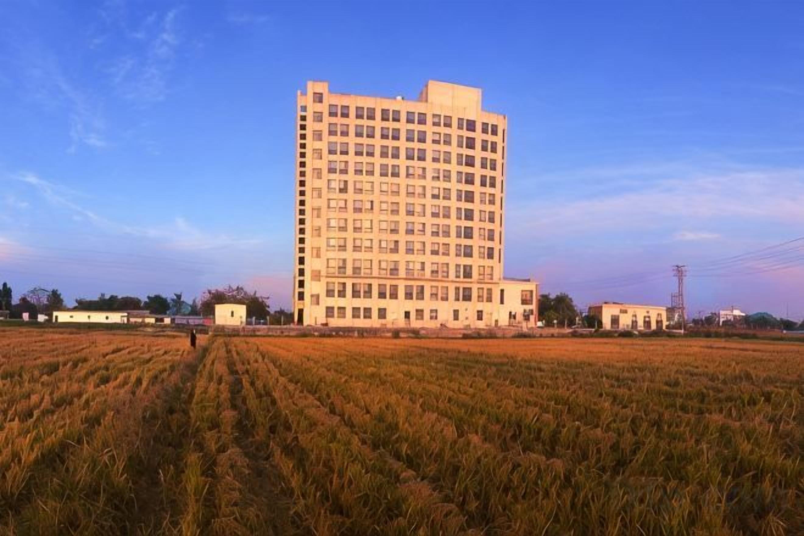 A large, multi-story building with a flat roof, surrounded by a field.