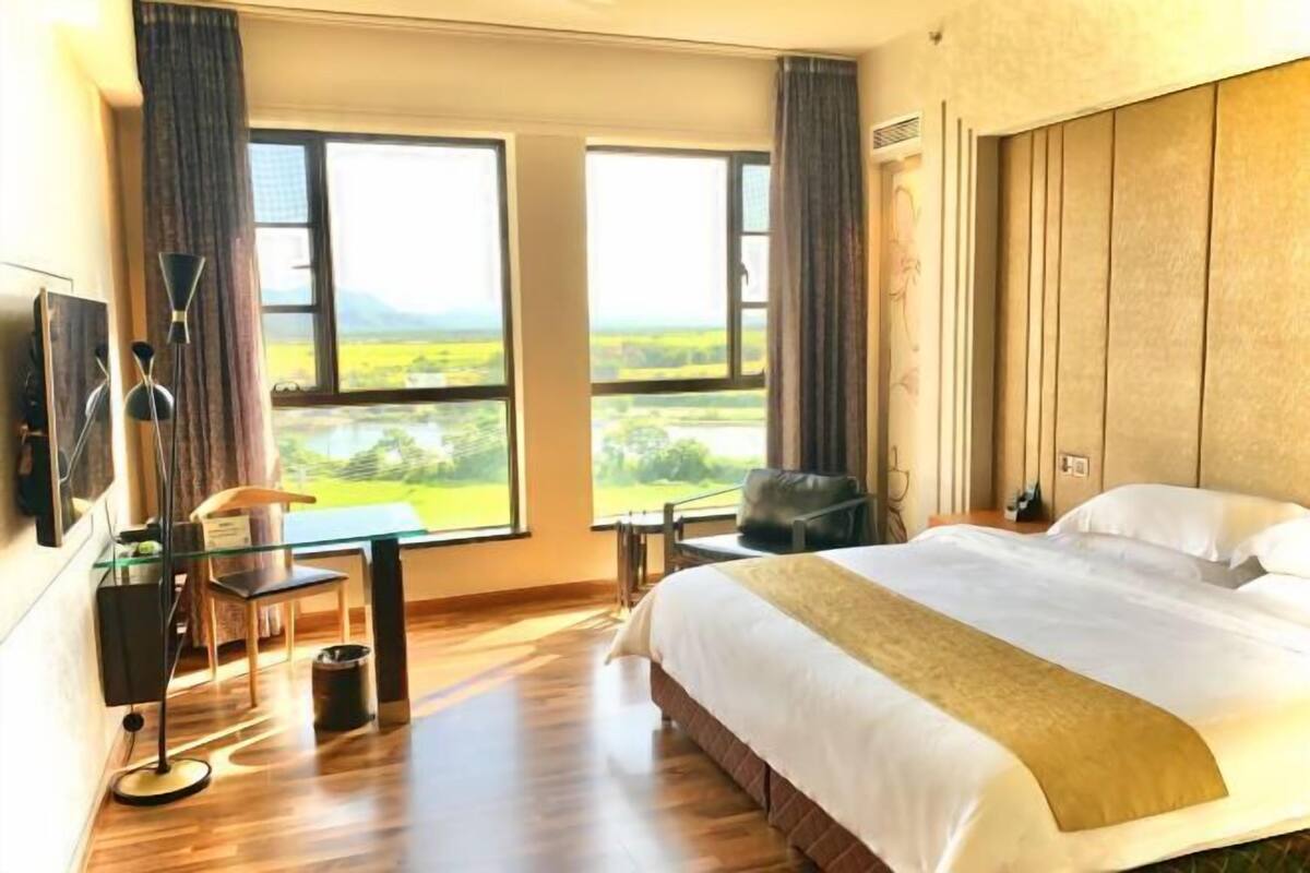 A hotel room with a large bed, a desk, a chair, and a view of the countryside.