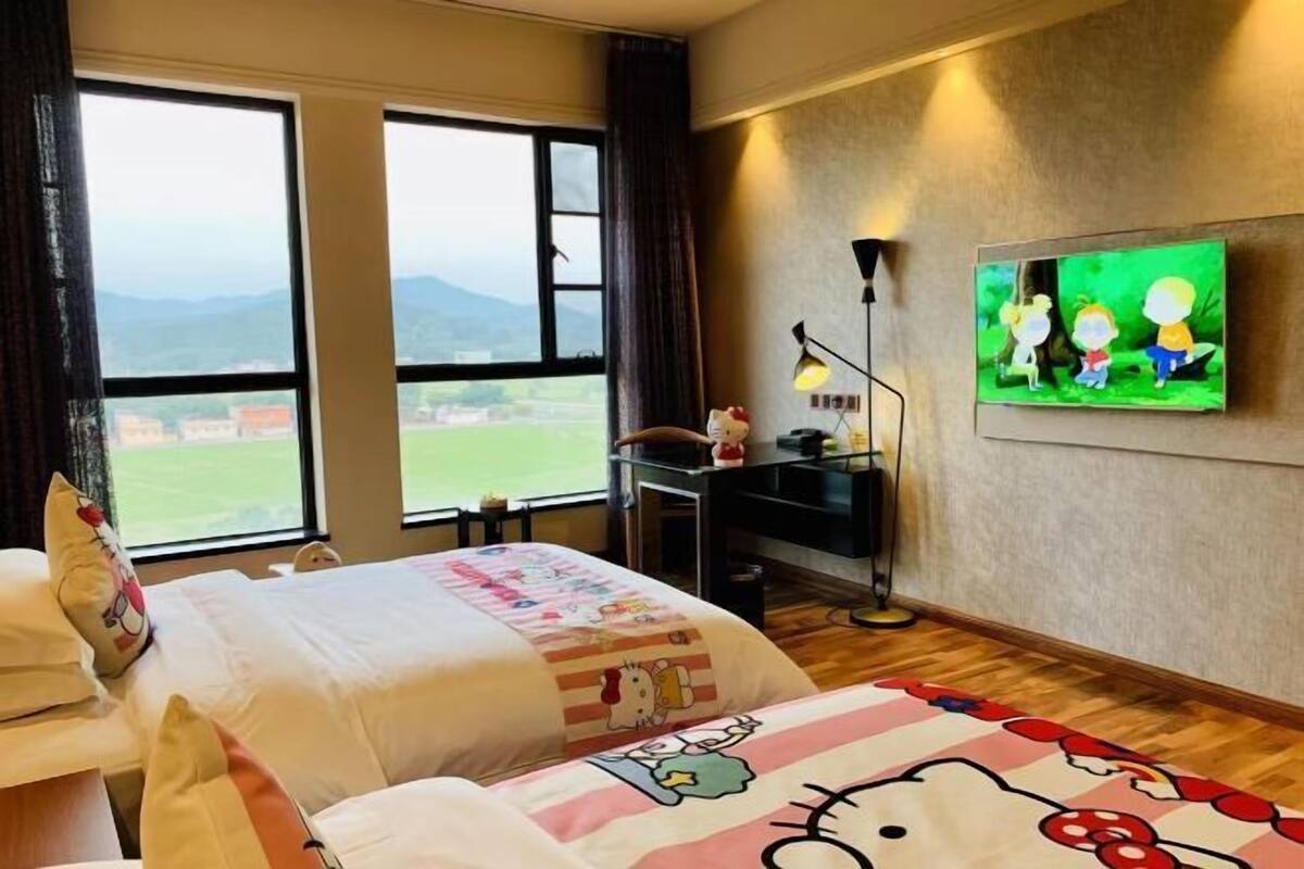 A hotel room with two beds, a desk, a TV, and a view of the outdoors.