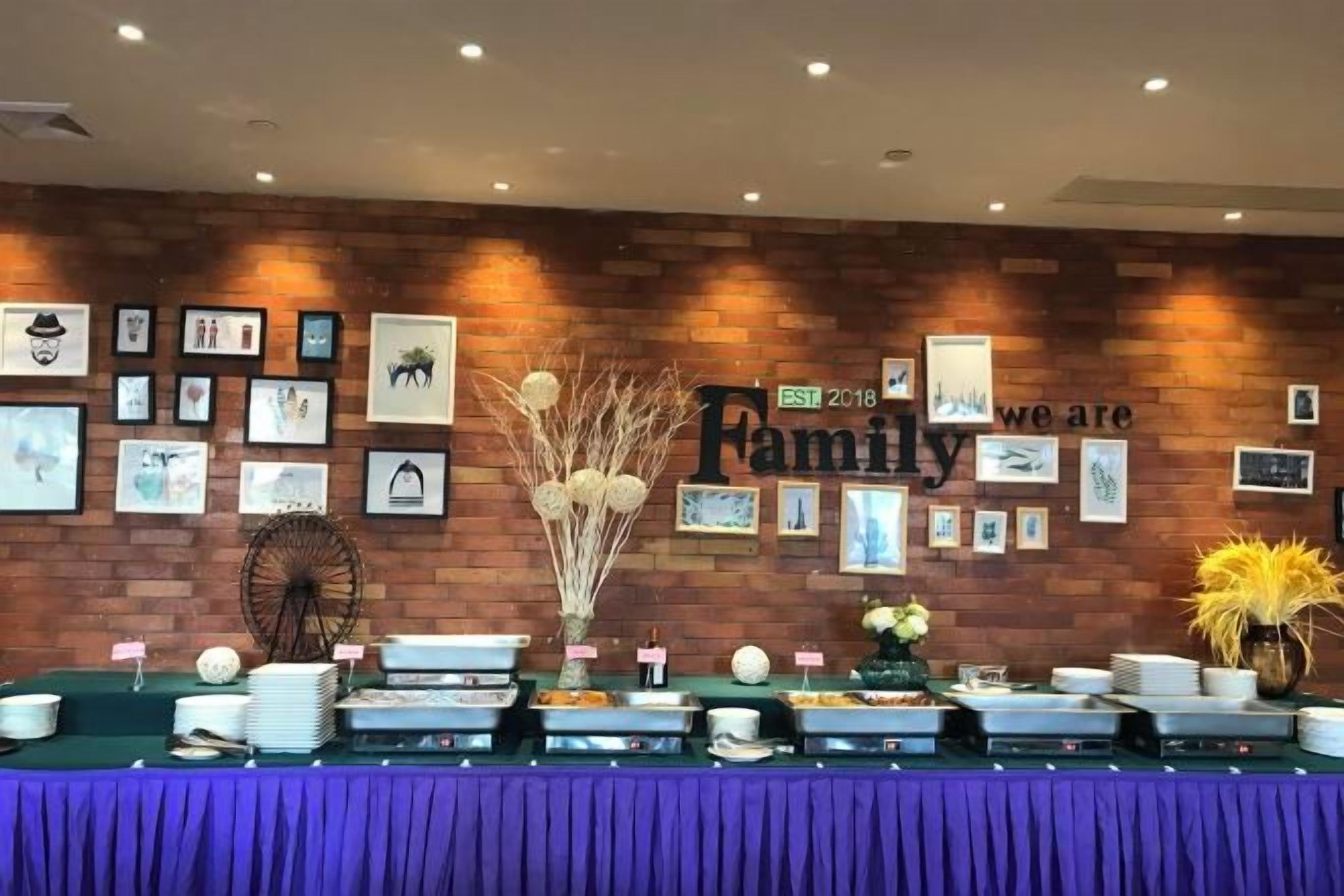 A buffet setup with a brick wall and framed pictures, a sign reading 'Family 2018', and a purple tablecloth.