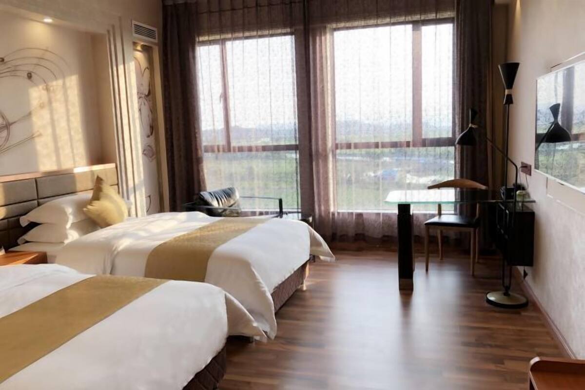 A hotel room with two beds, a desk, a chair, and a large window with a view.