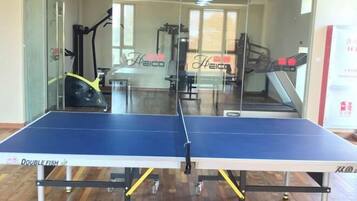 Une table de ping-pong avec un miroir sur un côté, du matériel d’exercice et une fenêtre avec des stores en arrière-plan.