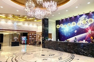 Un vestíbulo de hotel con un mostrador de recepción, un gran candelabro, un mural de espacio en la pared y un suelo con estampado.