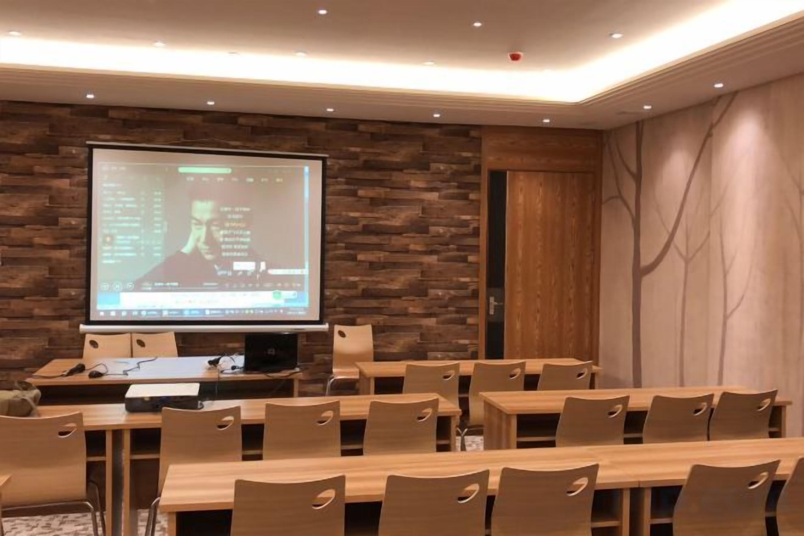A conference room with a large projection screen, wooden tables, and chairs.