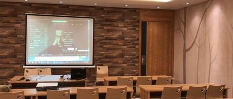 A conference room with a large projection screen, wooden tables, and chairs.