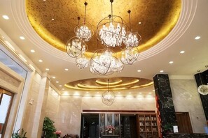 Een ruime lobby met een grote kroonluchter, marmeren wanden en een receptiebalie.