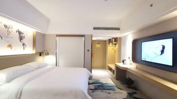 A hotel room with a large bed, a flat-screen TV mounted on the wall, a world map on the wall, and a small desk with a lamp.